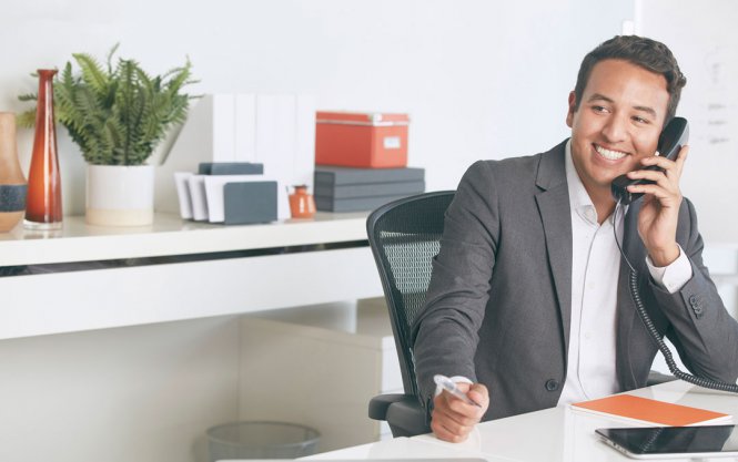A man sitting at a desk, talking on an office telephone.