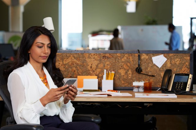 A woman using a smartphone while sitting at her desk.