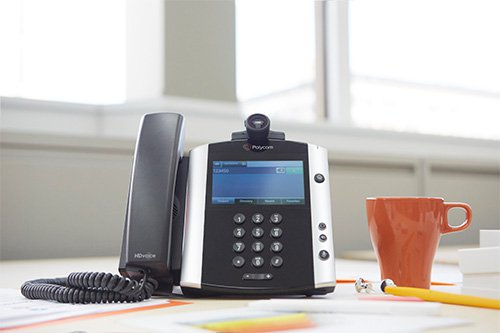 An office telephone on a desk next to a cup of coffee.