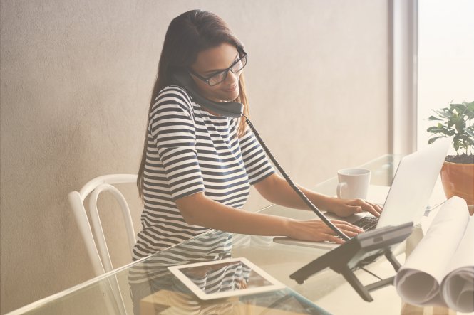 A woman sitting at her computer while talking on an office phone.