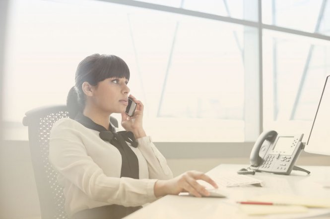A woman using her mobile phone at her desk, choosing a cloud provider.