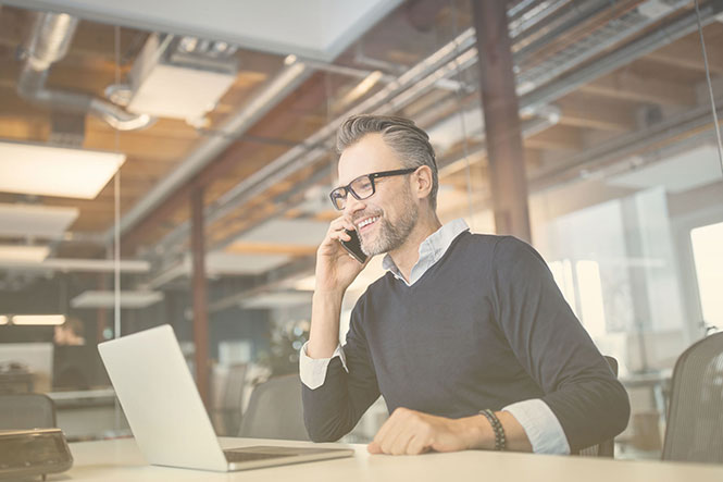 Person in office working on laptop and talking on smartphone — SIP definition