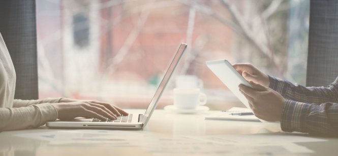 Two millennials use a laptop and tablet to access social media in healthcare