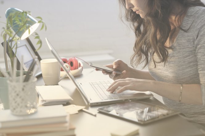 Female student at a desk with a laptop and smartphone engaging with student recruitment messages