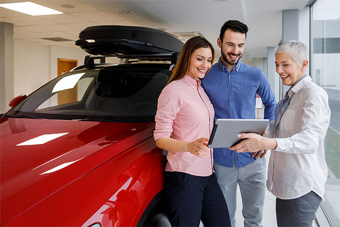 A car saleswoman uses car dealership mobility benefits on her tablet with a man and woman