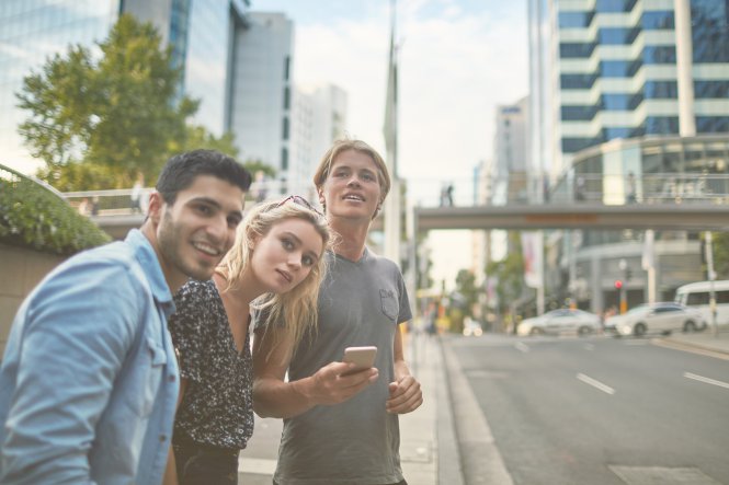 Three young people on a street in a new city using a phone where a hotel is marketing to millennials