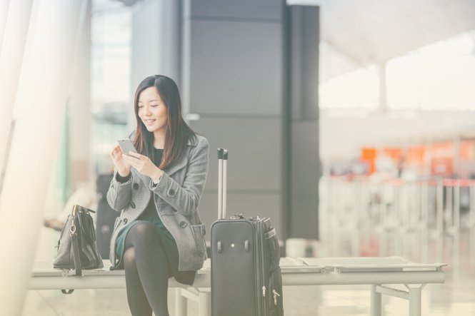 Traveling person in airport communicating with airline via travel itinerary API on smartphone