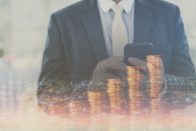 Person on smartphone in front of increasing coin stacks representing benefit of sales productivity