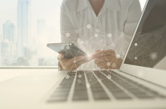 Person holding smartphone in front of a laptop and embracing the benefits of SIP trunking