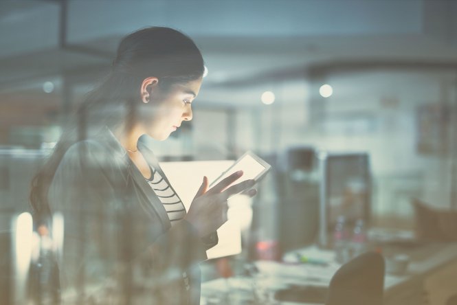 Person in office using tablet and standing in front of desks with computers — cloud migration