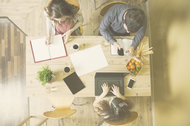 Three employees sitting at table working with smartphone, laptop, and paper — communication audit
