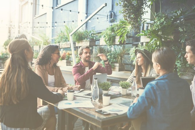 Group of employees sitting around table with computers and papers discussing UCaaS solutions