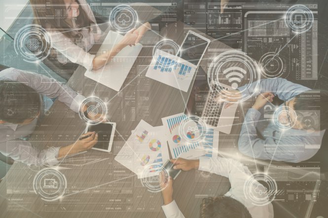 Four employees using cloud migration tools, laptops, and charts at conference table