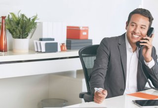 A man sitting at a desk, talking on an office telephone.