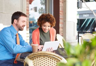 <p>A man and a woman sitting outside at a coffee shop, using a tablet.</p>