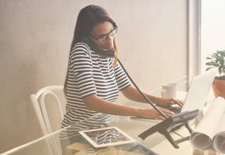 A woman sitting at her computer while talking on an office phone.