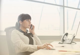 A woman using her mobile phone at her desk, choosing a cloud provider.