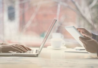 Two millennials use a laptop and tablet to access social media in healthcare