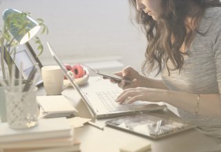 Female student at a desk with a laptop and smartphone engaging with student recruitment messages