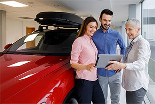 A car saleswoman uses car dealership mobility benefits on her tablet with a man and woman