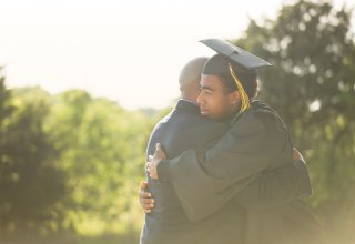 A young man who had an academic career enriched by mobile apps embraces his dad at graduation.