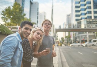 Three young people on a street in a new city using a phone where a hotel is marketing to millennials