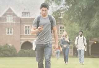 Student using flipped learning on smartphone and walking across campus with backpack on
