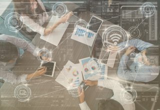 Four employees using cloud migration tools, laptops, and charts at conference table